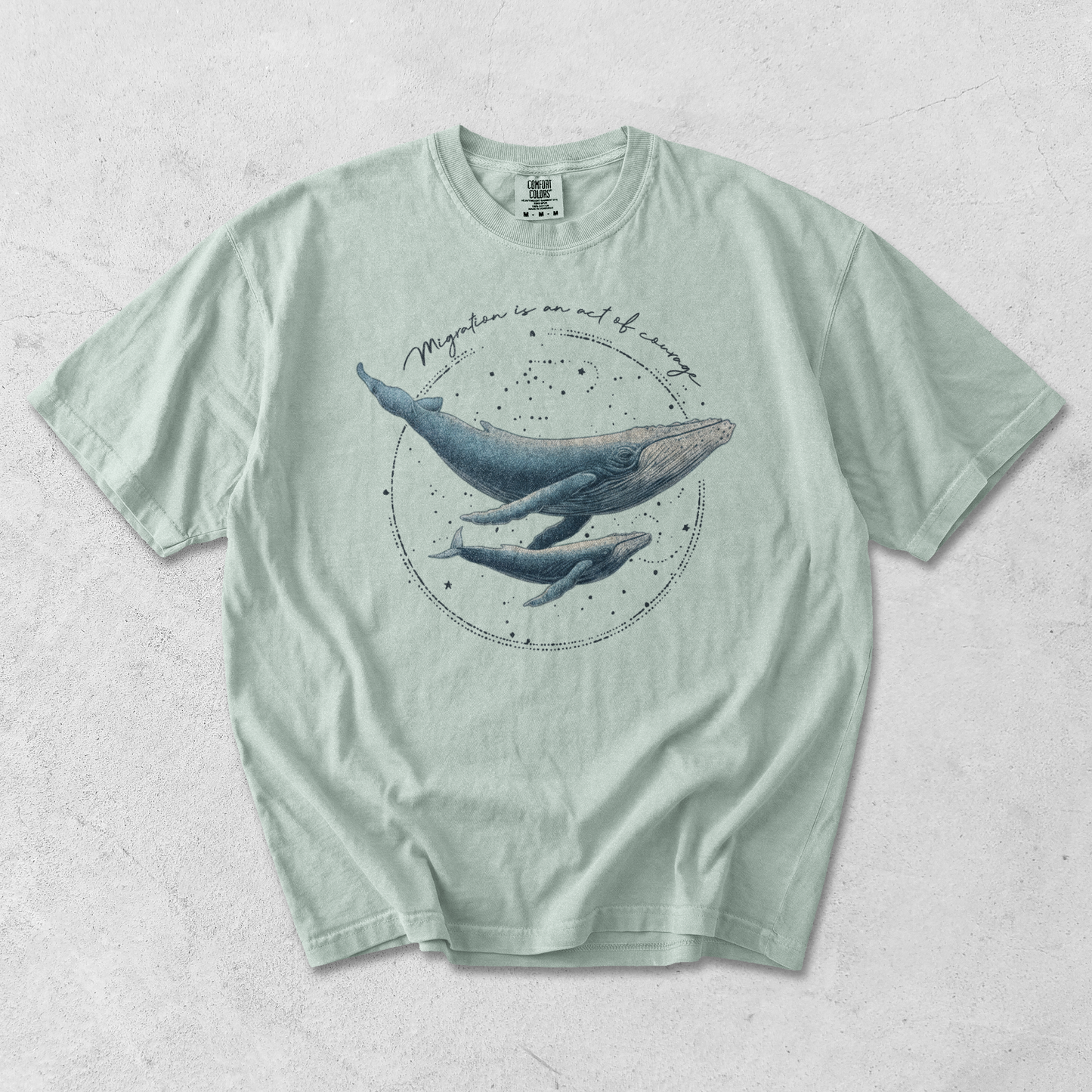 Mint green t-shirt with whale graphic on a textured surface, with writing migration is and act of courage
